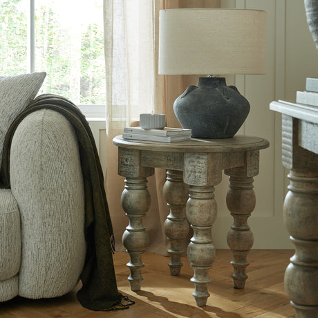 Hill Interiors Wooden Round Side Table in brown with four turned baluster legs, styled beside a sofa with a lamp, dark vase and books on top.