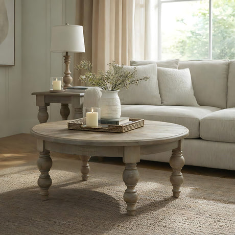 Hill Interiors Round Wooden Coffee Table in brown with turned legs, styled with a candle tray and vase in a neutral living room beside a cream sofa.