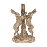 Close-up of the Hill Interiors Marching Hares table lamp base, showing two resin hares standing upright against a central tree trunk in a brown finish.