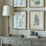 Hill Interiors candlestick table lamp with turned brown resin base and natural linen shade on a grey console beside framed botanical prints.