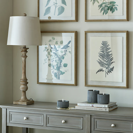 Hill Interiors candlestick table lamp with turned brown resin base and natural linen shade on a grey console beside framed botanical prints.