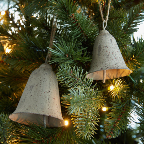 Hill Interiors Large Rustic Metal Hanging Bells in weathered brown, hung by jute twine among lit Christmas tree branches.