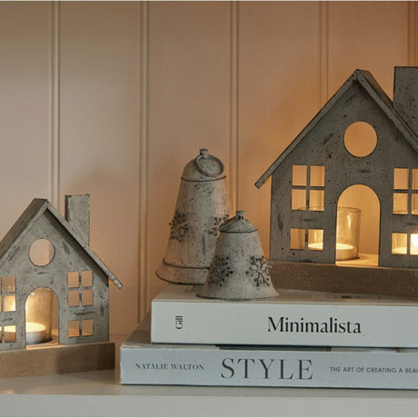 Hill Interiors rustic white metal hanging bells with snowflake motifs, displayed on stacked style books beside wooden house tealight lanterns.