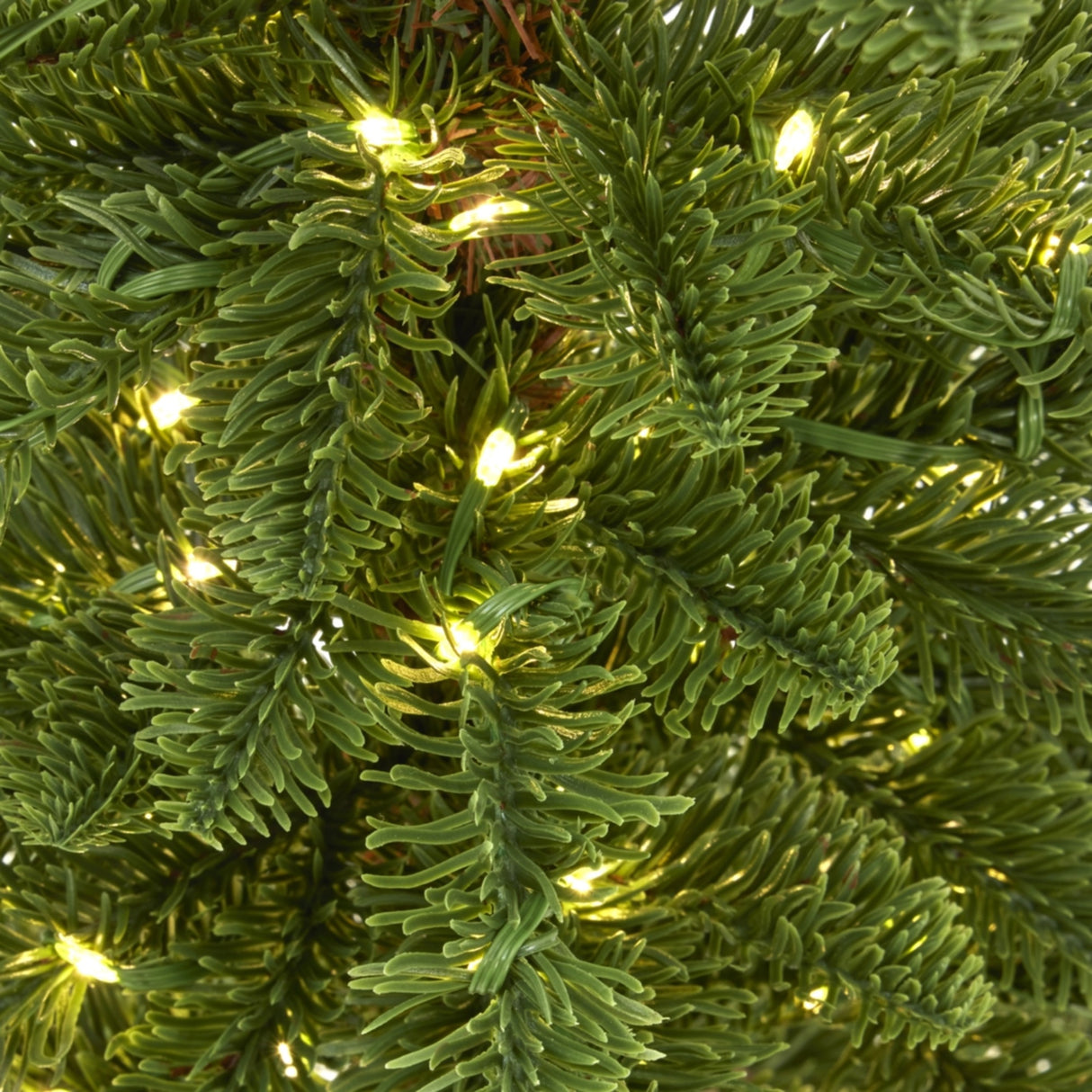 Close-up of Hill Interiors Medium Woodland Christmas Tree branches, showing dense green plastic tips with pre-fitted warm white LED lights glowing throughout.