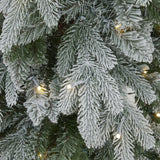 Close-up of Hill Interiors Slim Snowy Woodland Christmas tree branches with snow-dusted plastic needles and warm white LEDs woven through the foliage.