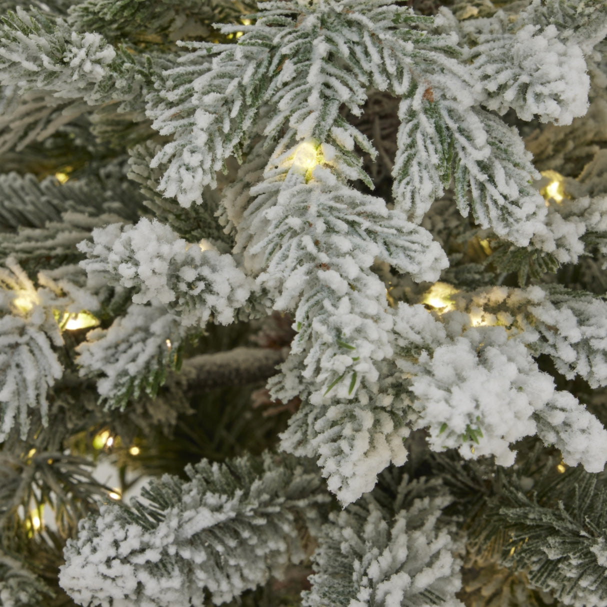 Close-up of Hill Interiors Snowy Forest Fir pre-lit Christmas tree showing frosted green plastic branches interwoven with warm white LED lights.