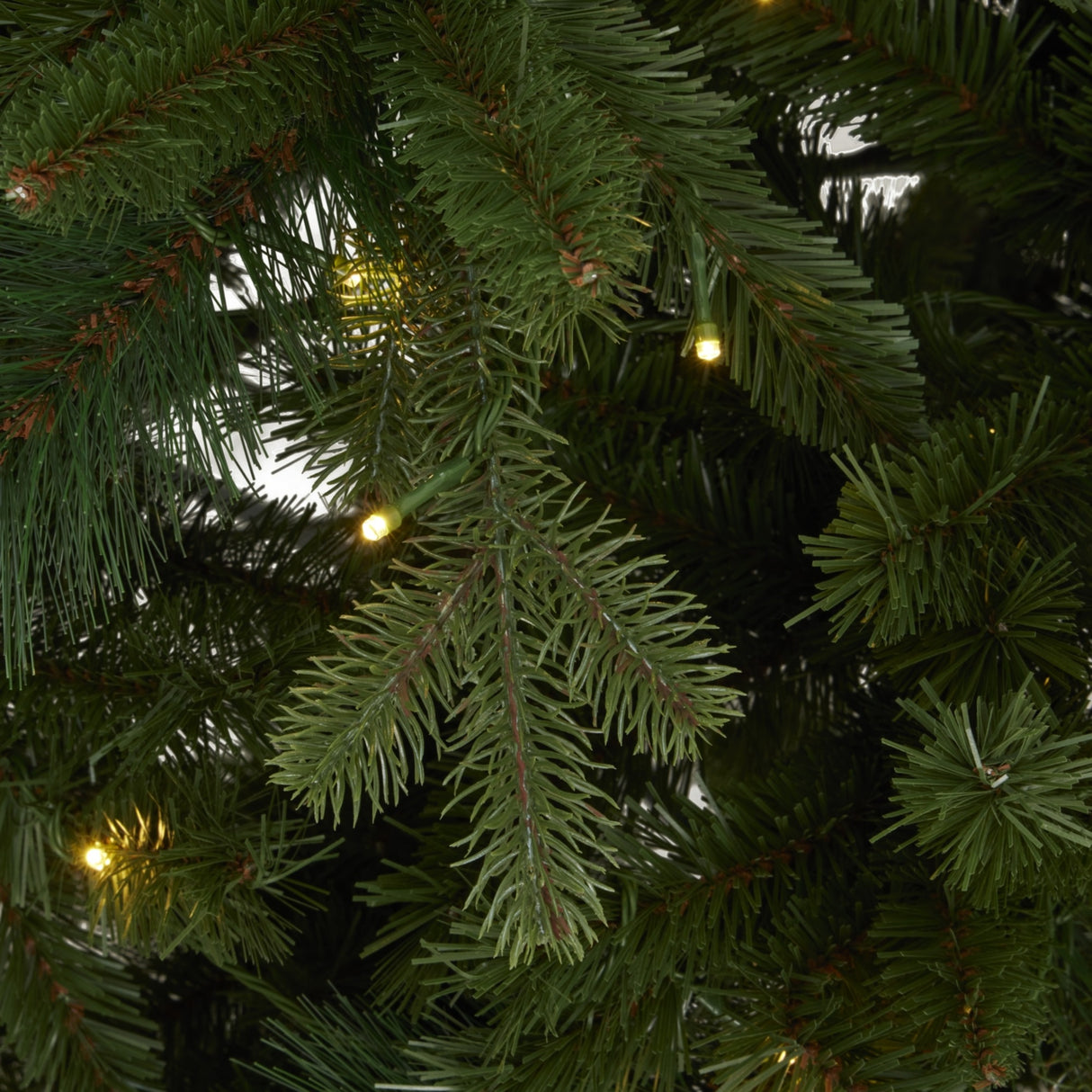 Close-up of Hill Interiors Fir 400L LED Christmas Tree in green, showing dense plastic needle branches with warm white pre-wired LEDs glowing softly.