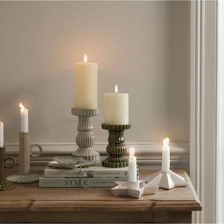 Hill Interiors Ceramic Angled Star Candle Holder in white, holding a lit taper on a wooden console beside books, pillar candles on ceramic stands, and tapers.