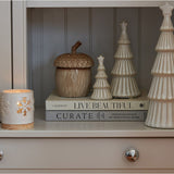 Hill Interiors large white ceramic snowy layered Christmas tree with star topper, displayed on stacked books beside an acorn jar and snowflake candle holder.