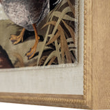 Close-up of Hill Interiors Duck on Linen Print showing the bird's orange feet among grasses, glass front and beaded wooden frame edge in brown tones.