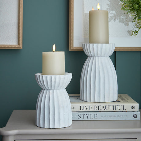 Two white fluted glass candle holders by Hill Interiors with lit pillar candles, styled on a console with books, framed art and greenery.