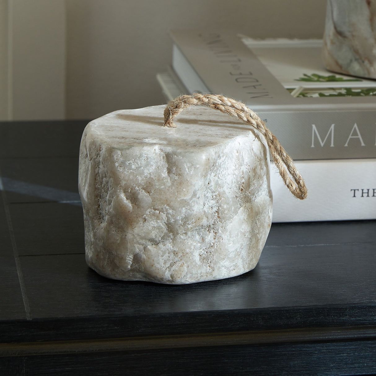Hill Interiors Marble Doorstop in white with soft grey veining and a jute rope handle, styled on a dark wooden surface beside stacked books.