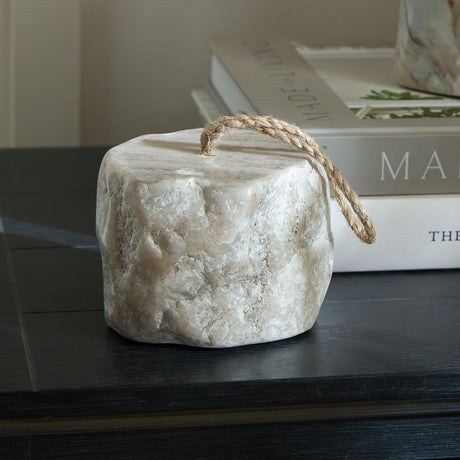 Hill Interiors Marble Doorstop in white with soft grey veining and a jute rope handle, styled on a dark wooden surface beside stacked books.
