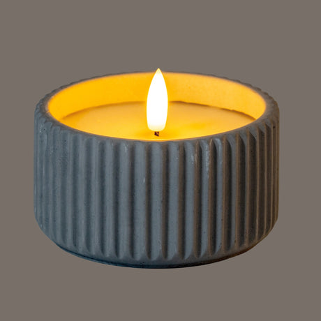 Hill Interiors Ribbed LED Pillar Candle in beige wax with vertical ribbed texture and glowing flame-effect tip, shown on a grey background.