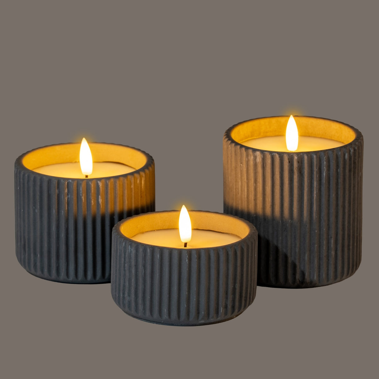 Hill Interiors Ribbed LED Pillar Candles in beige wax with chalky vertical ribbing, shown as a trio at varied heights with lit flameless wicks.