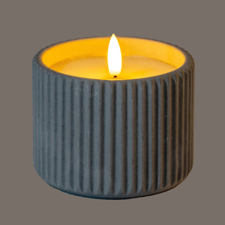 Hill Interiors ribbed chalk-finish LED pillar candle in beige wax with a flame-effect glow, shown on a plain grey background.