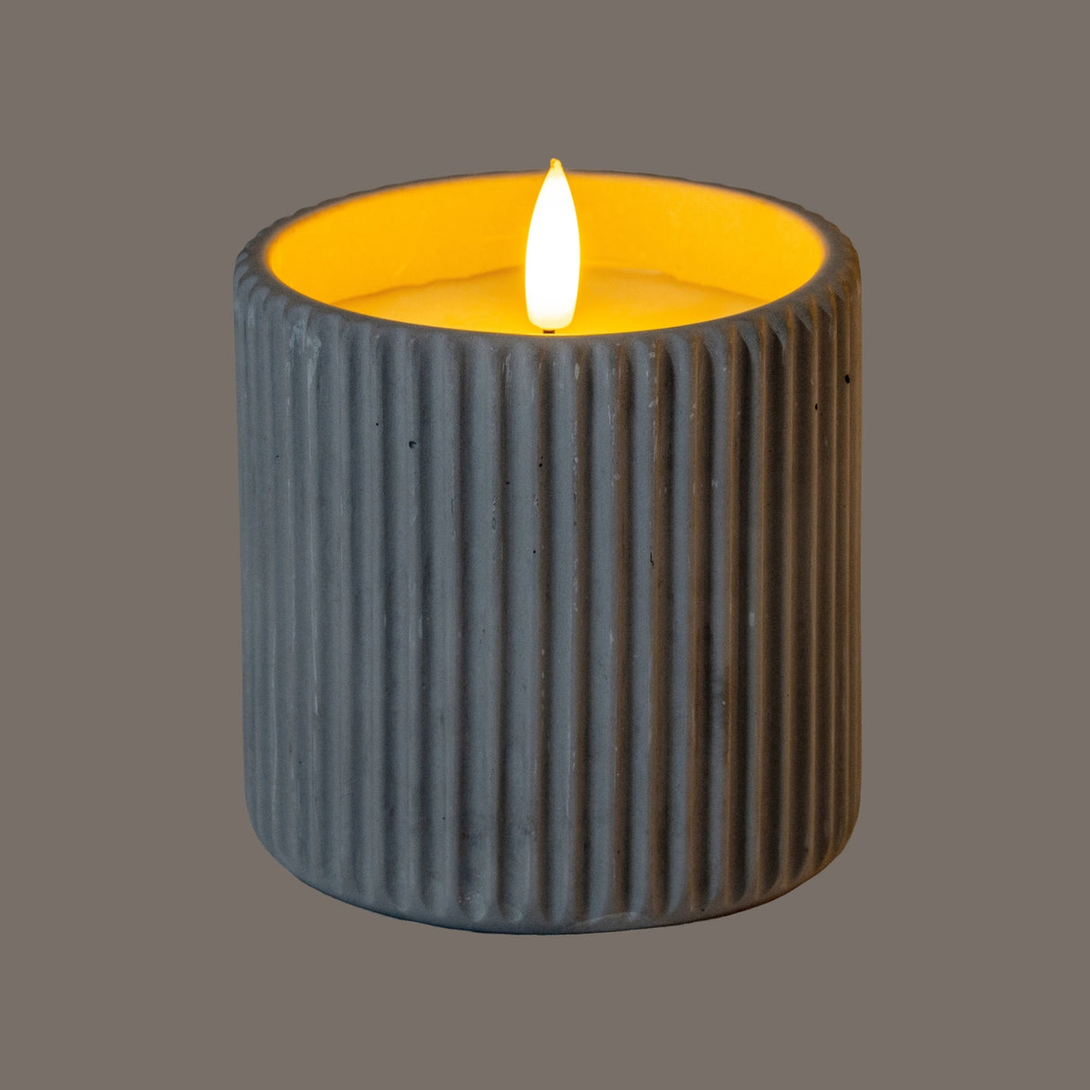 Hill Interiors Ribbed LED Pillar Candle in beige wax with vertical ribbed texture and glowing flame-effect light, shown against a grey background.