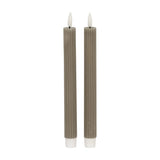 Hill Interiors Ribbed Taper Candles in beige, a pair of slim vertically ribbed wax tapers with lit flame tips, shown on a plain white background.