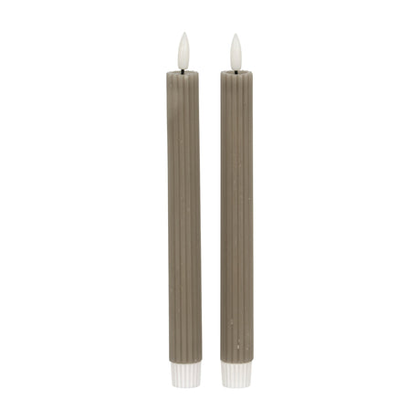 Hill Interiors Ribbed Taper Candles in beige, a pair of slim vertically ribbed wax tapers with lit flame tips, shown on a plain white background.