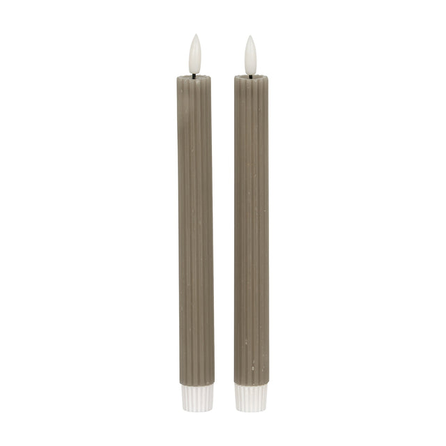 Hill Interiors Ribbed Taper Candles in beige, a pair of slim vertically ribbed wax tapers with lit flame tips, shown on a plain white background.