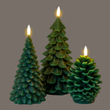 Hill Interiors Natural Glow LED wax candles in green, shaped as two fir trees and a pine cone with lit flame-effect tips, on a grey background.