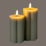 Hill Interiors Natural Glow LED pillar candles in beige, two fluted plastic pillars of differing heights with flickering LED flames on a grey background.