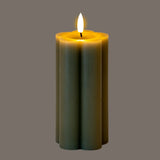 Hill Interiors Natural Glow LED pillar candle in beige plastic with a scalloped fluted shape and flickering flame effect, shown on a grey background.