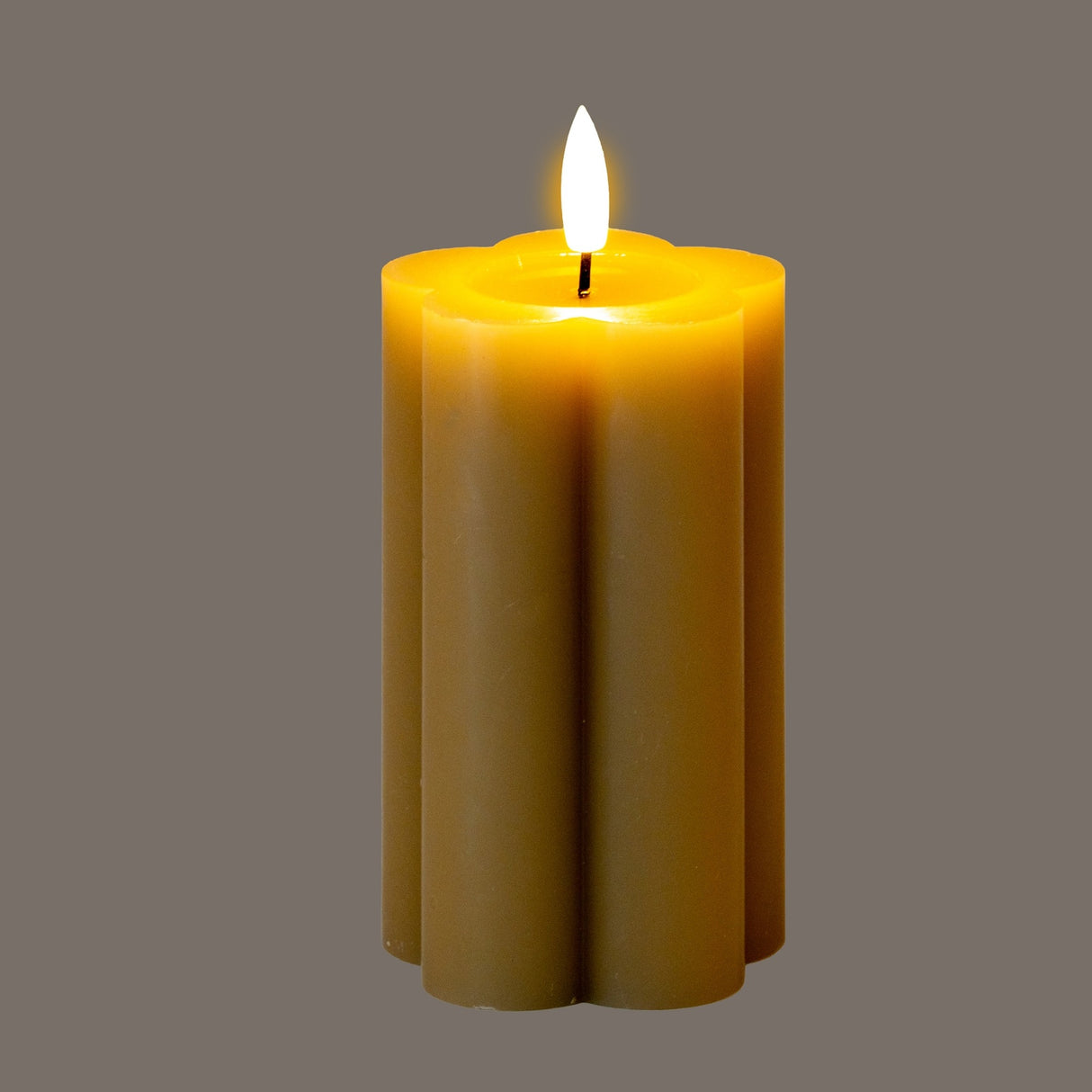 Hill Interiors Natural Glow beige stone-effect LED pillar candle with scalloped fluted sides and flickering flame, shown on a grey background.