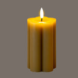 Hill Interiors Natural Glow beige stone-effect LED pillar candle with scalloped fluted sides and flickering flame, shown on a grey background.