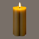 Hill Interiors Natural Glow beige LED pillar candle with fluted stone effect body and amber flicker flame, shown against a grey background.