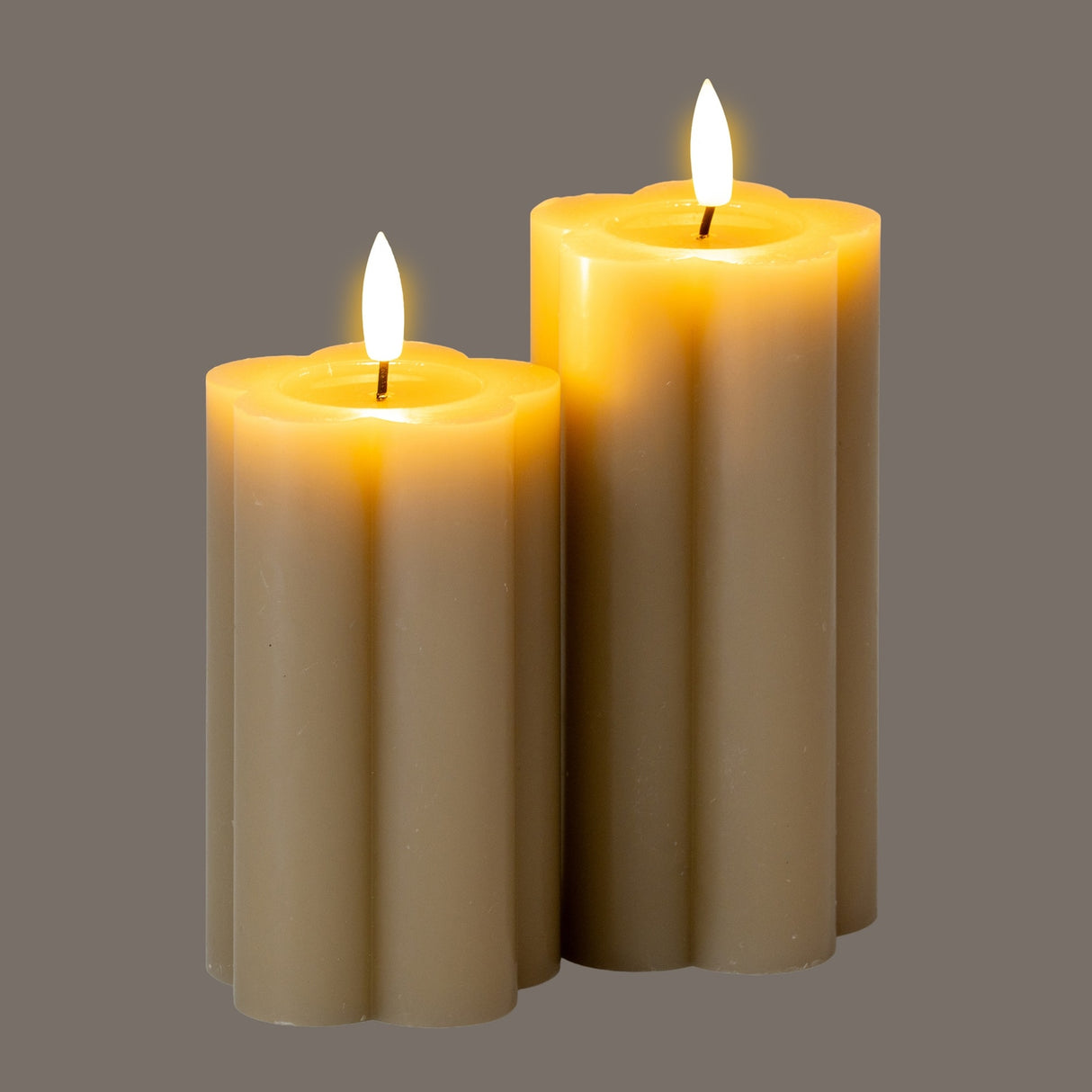 Hill Interiors Natural Glow beige LED pillar candles in two heights with fluted stone effect finish and amber flame tips, shown on a grey background.