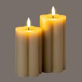 Hill Interiors Natural Glow beige LED pillar candles in two heights with fluted stone effect finish and amber flame tips, shown on a grey background.