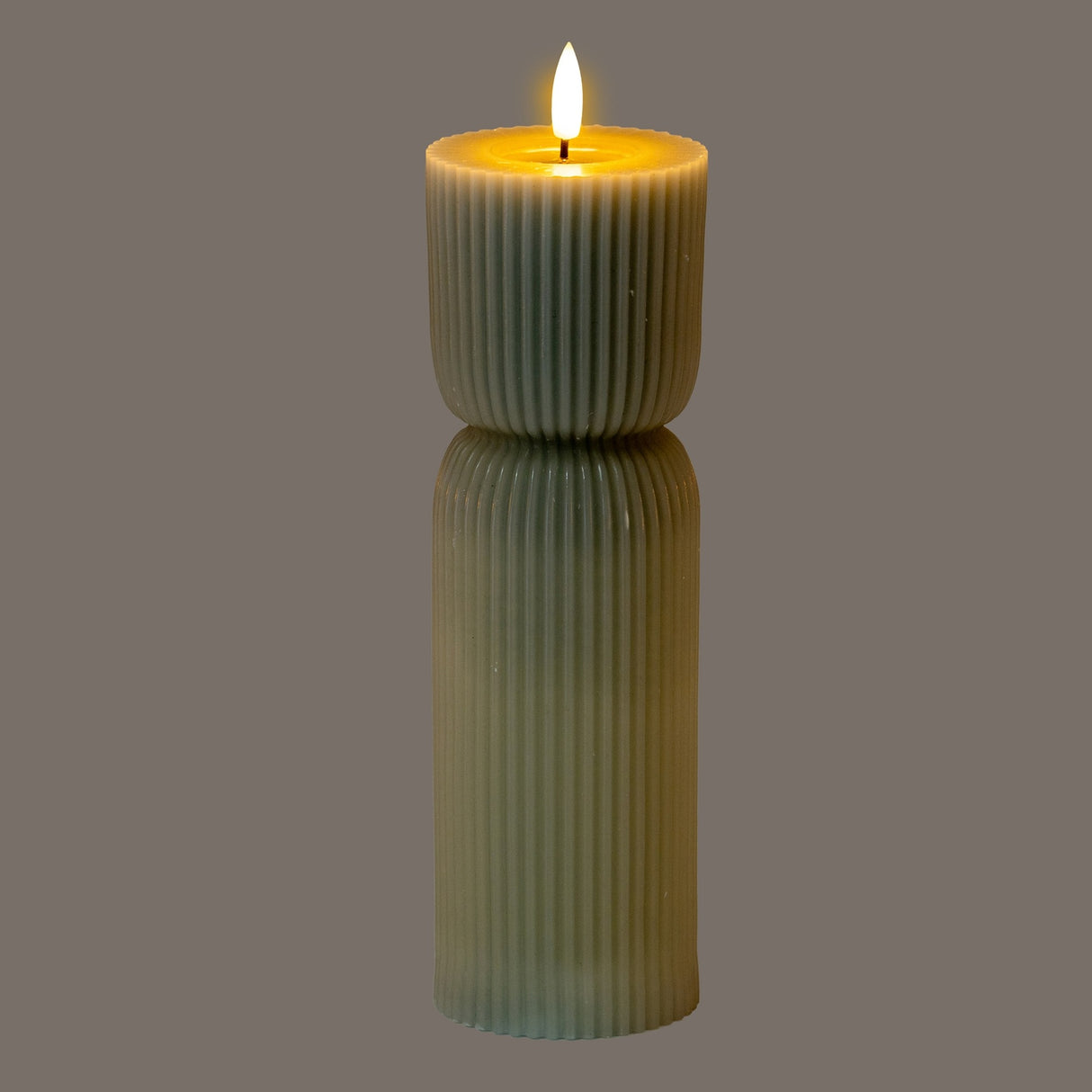 Hill Interiors Natural Glow carved LED pillar candle in beige, with ribbed plastic body and lit flame-effect tip, shown on a grey background.