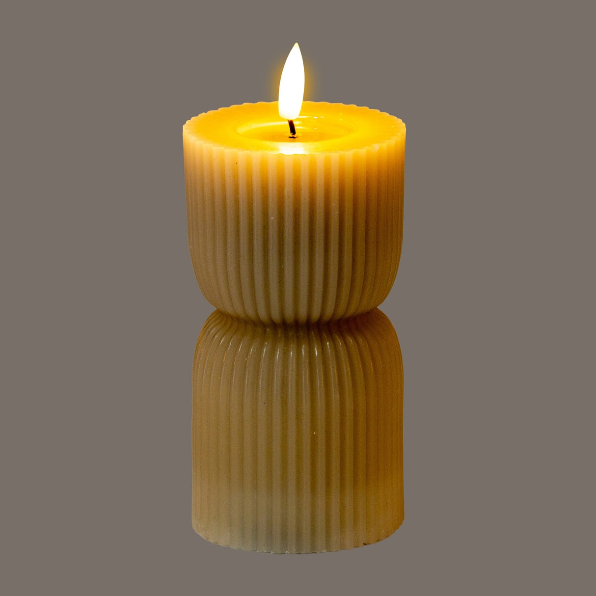Hill Interiors Stone Carved LED Pillar Candle in beige with ribbed fluted texture and flickering flame, shown on a reflective grey surface.