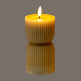Hill Interiors Stone Carved LED Pillar Candle in beige with ribbed fluted texture and flickering flame, shown on a reflective grey surface.
