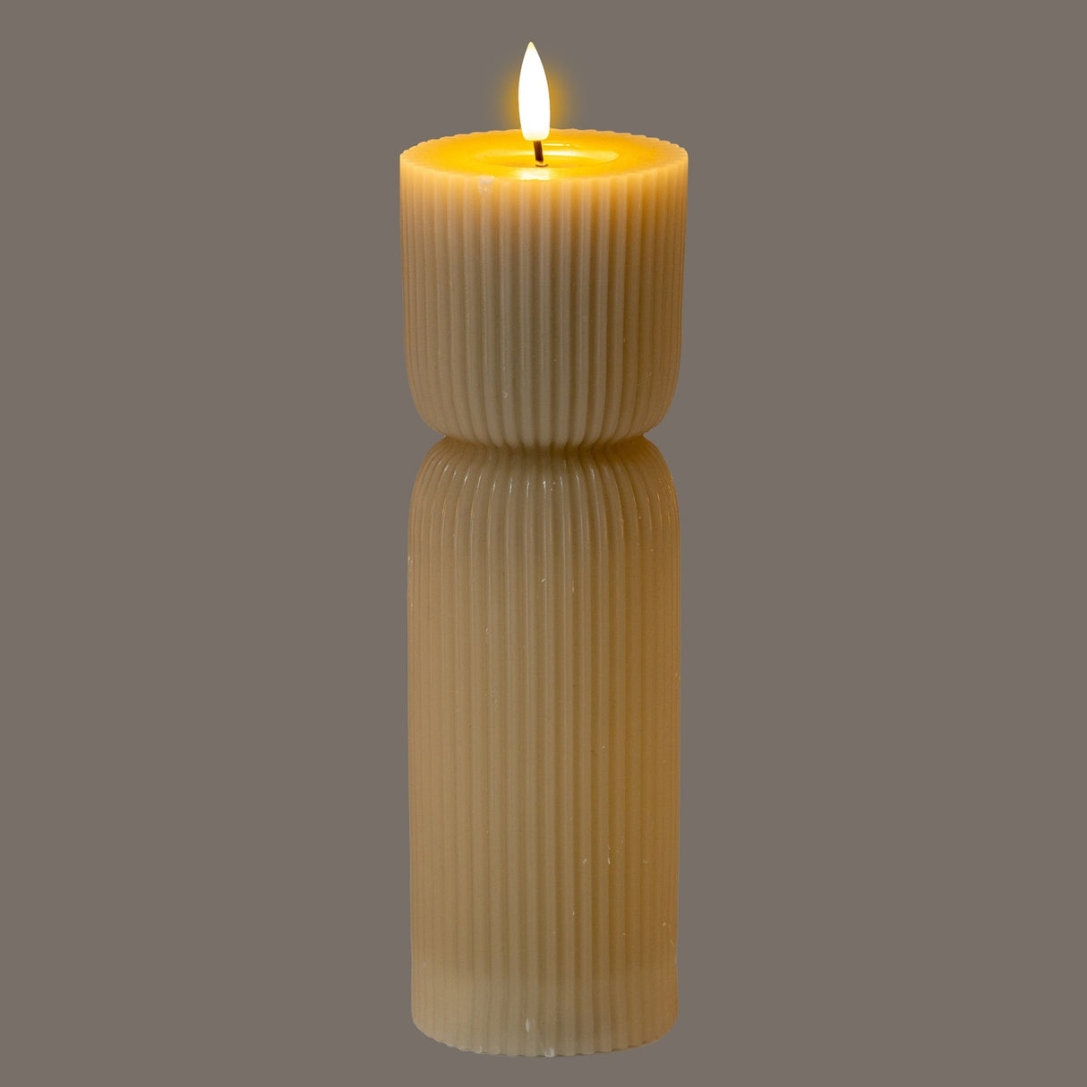 Hill Interiors Natural Glow beige LED pillar candle with ribbed stone-carved texture and flickering flame, shown on a grey background.
