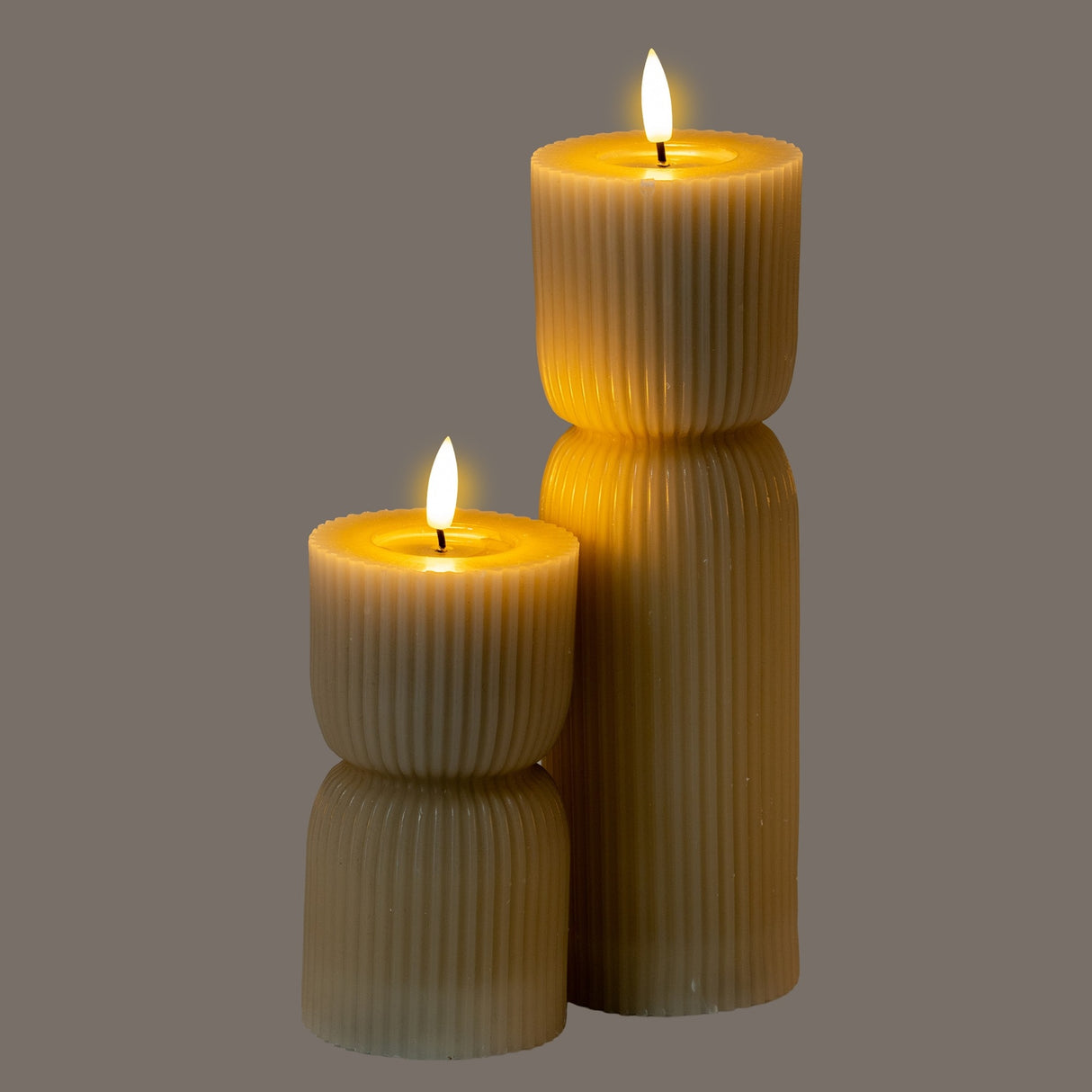 Hill Interiors Natural Glow beige LED pillar candles with ribbed stone-effect finish and flickering flames, shown in two heights on a grey background.