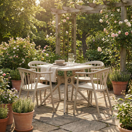 Hill Interiors Moulded Plastic Accent Chairs in beige around a matching table on a sunlit garden patio framed by roses, potted herbs and a wooden pergola.