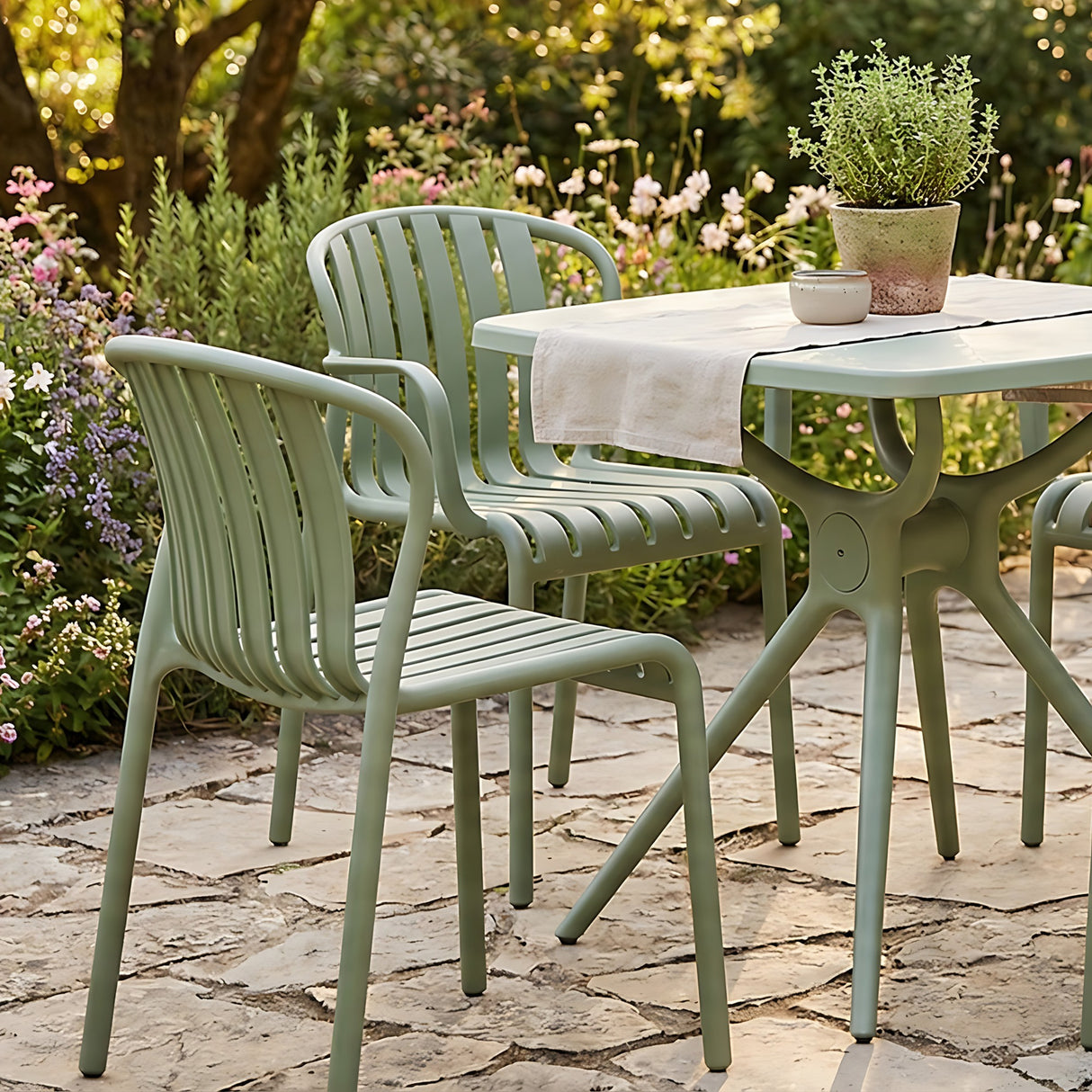 Hill Interiors Moulded Plastic Accent Chairs in French grey with slatted backs and armrests, paired with a matching garden table on a stone patio.