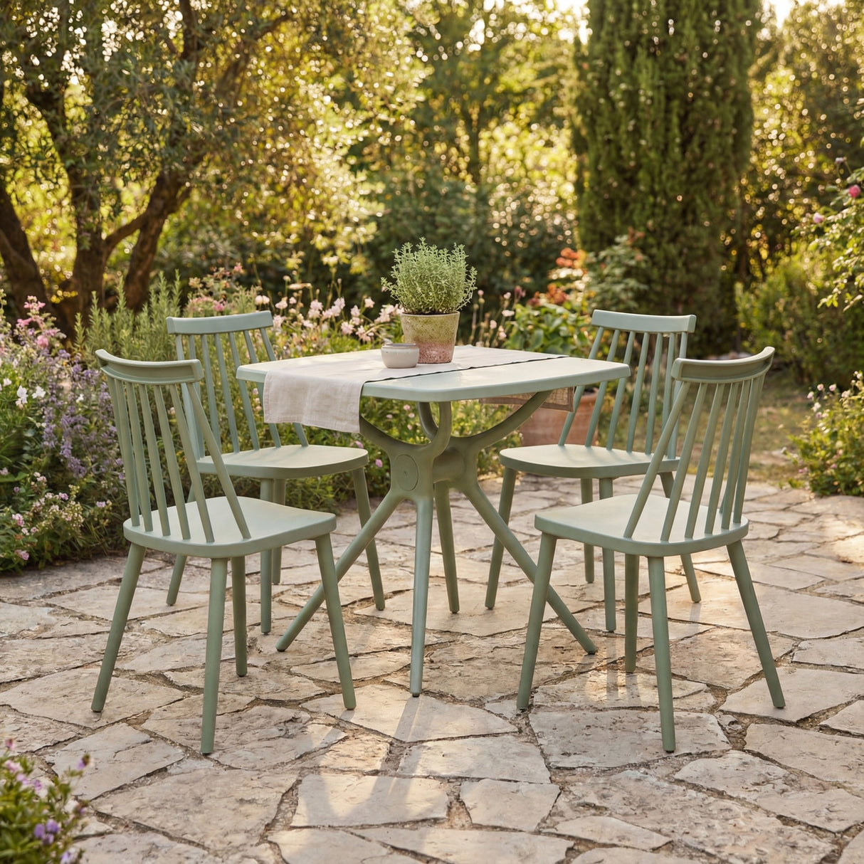 Hill Interiors Brolvanic dining set with four green spindle-back plastic chairs around a matching table on a garden stone patio.
