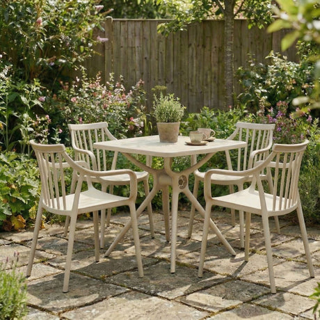 Hill Interiors beige plastic dining set with square table and four spindle-back armchairs on a garden patio surrounded by flowering borders.