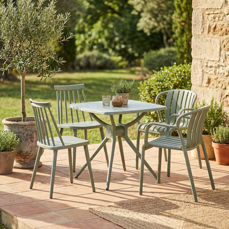 Hill Interiors French Grey side table and matching spindle-back chairs set on a terracotta terrace beside potted olive and herb plants.