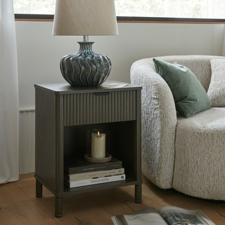 Hill Interiors 1 Drawer Wooden Cabinet in brown beside a boucle armchair, styled with a ceramic lamp, candle and stacked books on the open shelf.