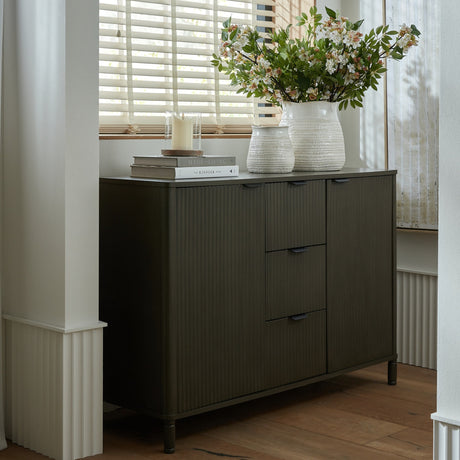 Hill Interiors 3 Drawer 2 Door Wooden Cabinet in brown with ribbed fronts, styled in a bright room with books, white vases and florals on top.