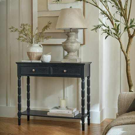 Hill Interiors 2 Drawer Console Table with Curved Frame in black, styled in a hallway with a lamp, vase and books on the lower shelf.