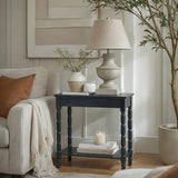 Hill Interiors Contoured Wooden Console Table in black with turned legs and lower shelf, styled in a living room with a lamp, vase and candle.