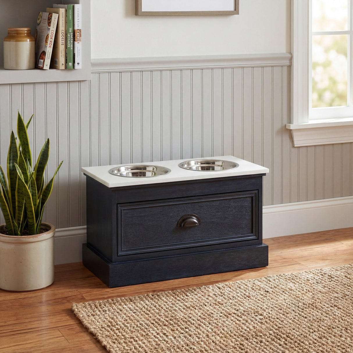 Hill Interiors wooden pet feeder table in black with white top and two stainless steel bowls, styled in a hallway with wainscoting and a snake plant.