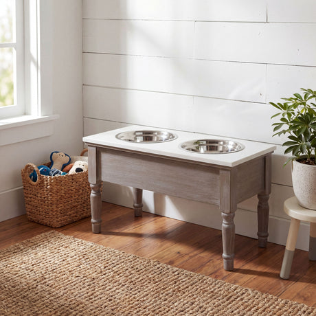 Hill Interiors Wooden Pet Feeder Table in grey with two stainless steel bowls, styled in a bright corner with a toy basket and potted plant.