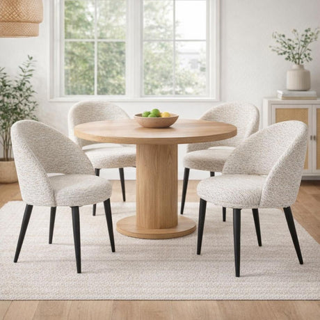 Hill Interiors Marlenza Curved Dining Chairs in white bouclé with black tapered legs, set around a round oak pedestal table in a bright dining room.