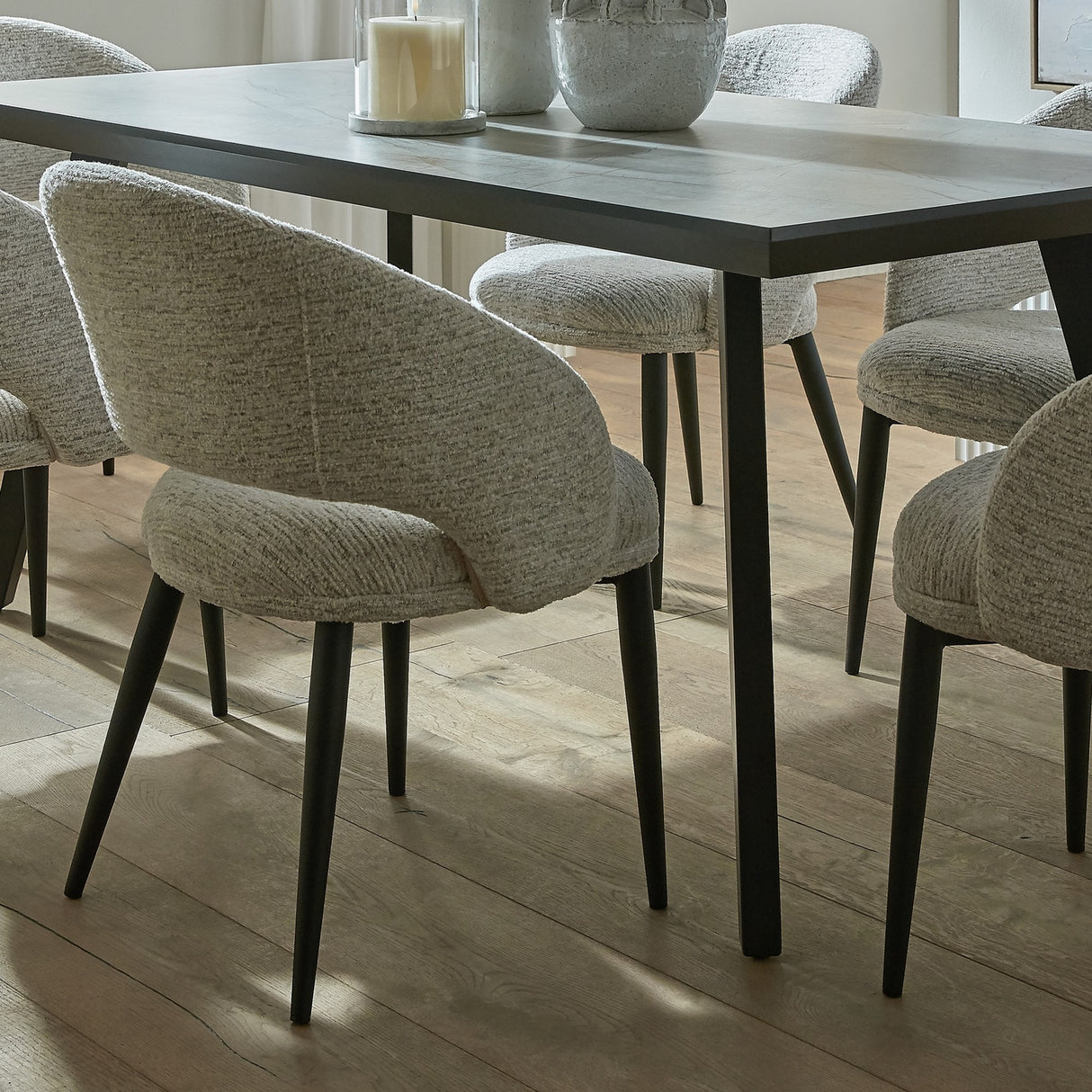 Hill Interiors Marlenza Curved Dining Chairs in neutral textured upholstery with black tapered legs, around a dark rectangular dining table on wood flooring.